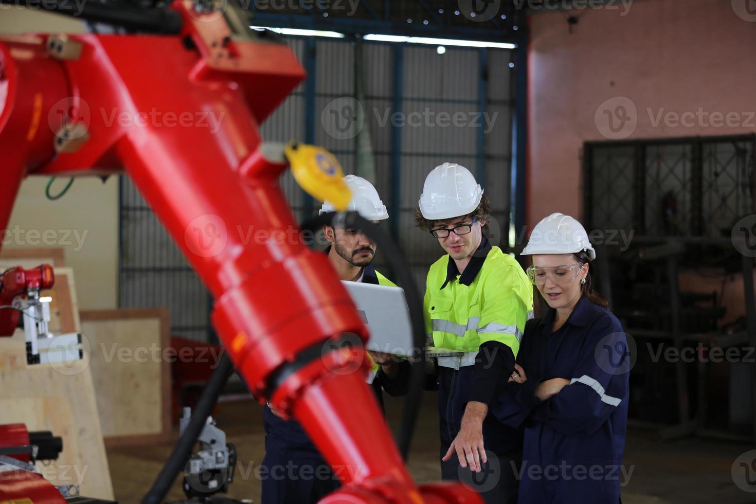 trois ingénieurs et ouvriers multiculturels de l'industrie lourde dans un bras de robot automatique à contrôle uniforme pour l'utilisation en usine. l'entrepreneur industriel féminin utilise une tablette. photo