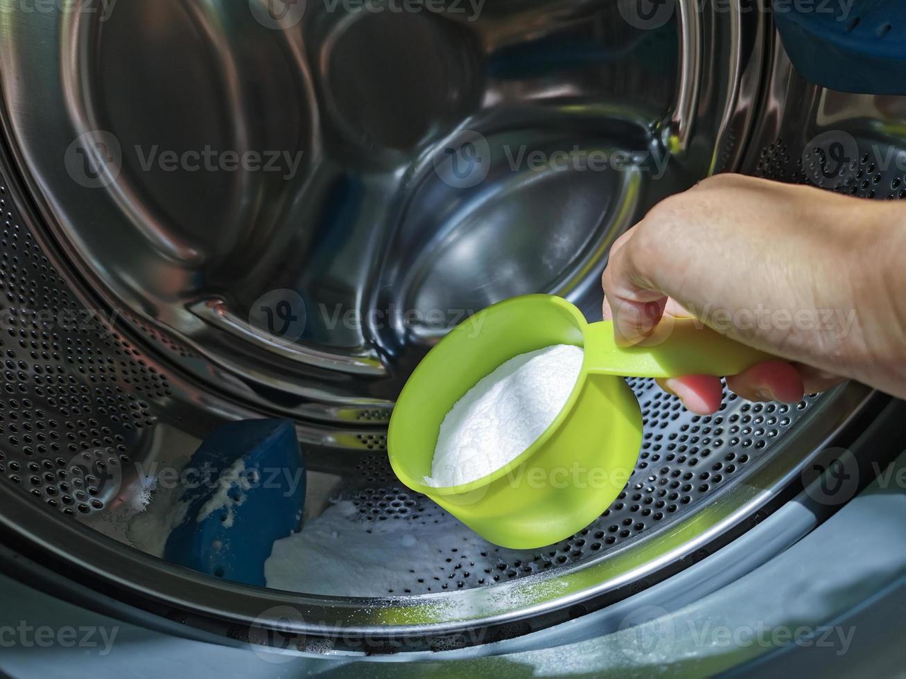 main en gros plan ajoutant de la poudre de bicarbonate de soude dans la machine à laver à chargement frontal pour nettoyer l'intérieur du tambour de la laveuse. photo