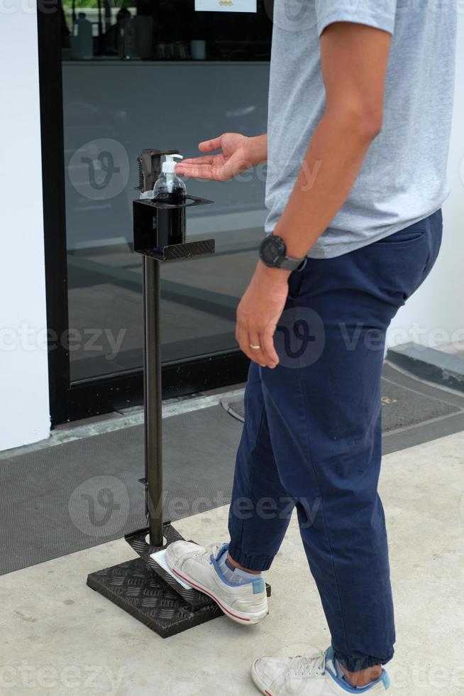 photo en gros plan d'un homme utilisé un distributeur de désinfectant pour les mains à commande au pied ou un support de désinfectant mains libres dans la zone pubienne. équipement sans contact. nettoyer et protéger contre le covid-19, la maladie du virus corona.