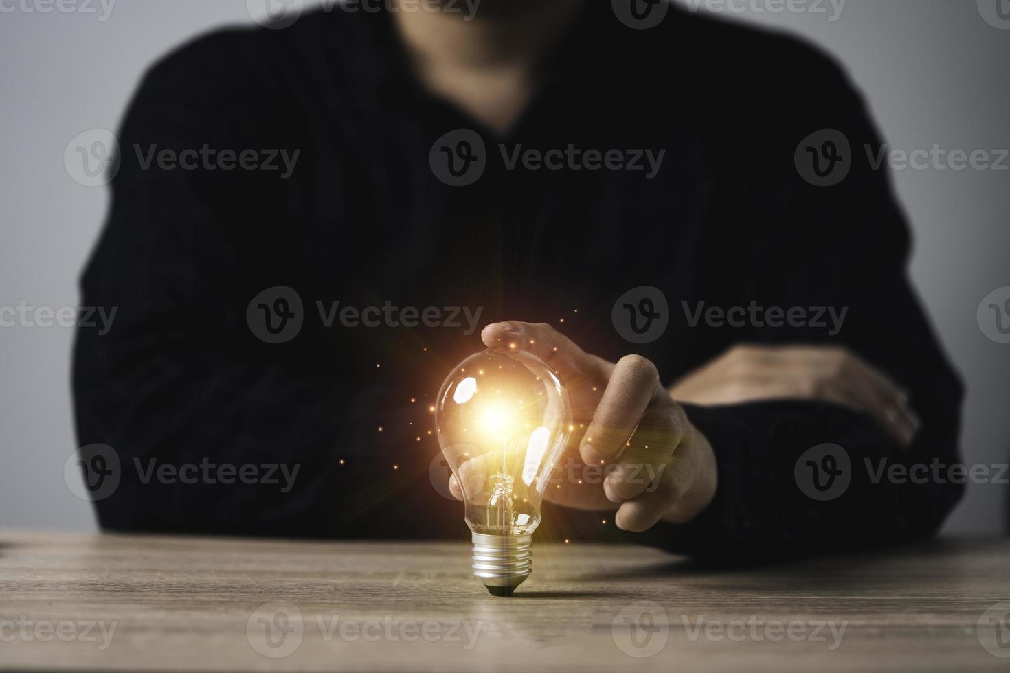 homme d'affaires tenant une ampoule rougeoyante avec un rayon lumineux orange sur une table en bois pour inspirer une idée de pensée créative et un futur concept de technologie d'innovation. photo