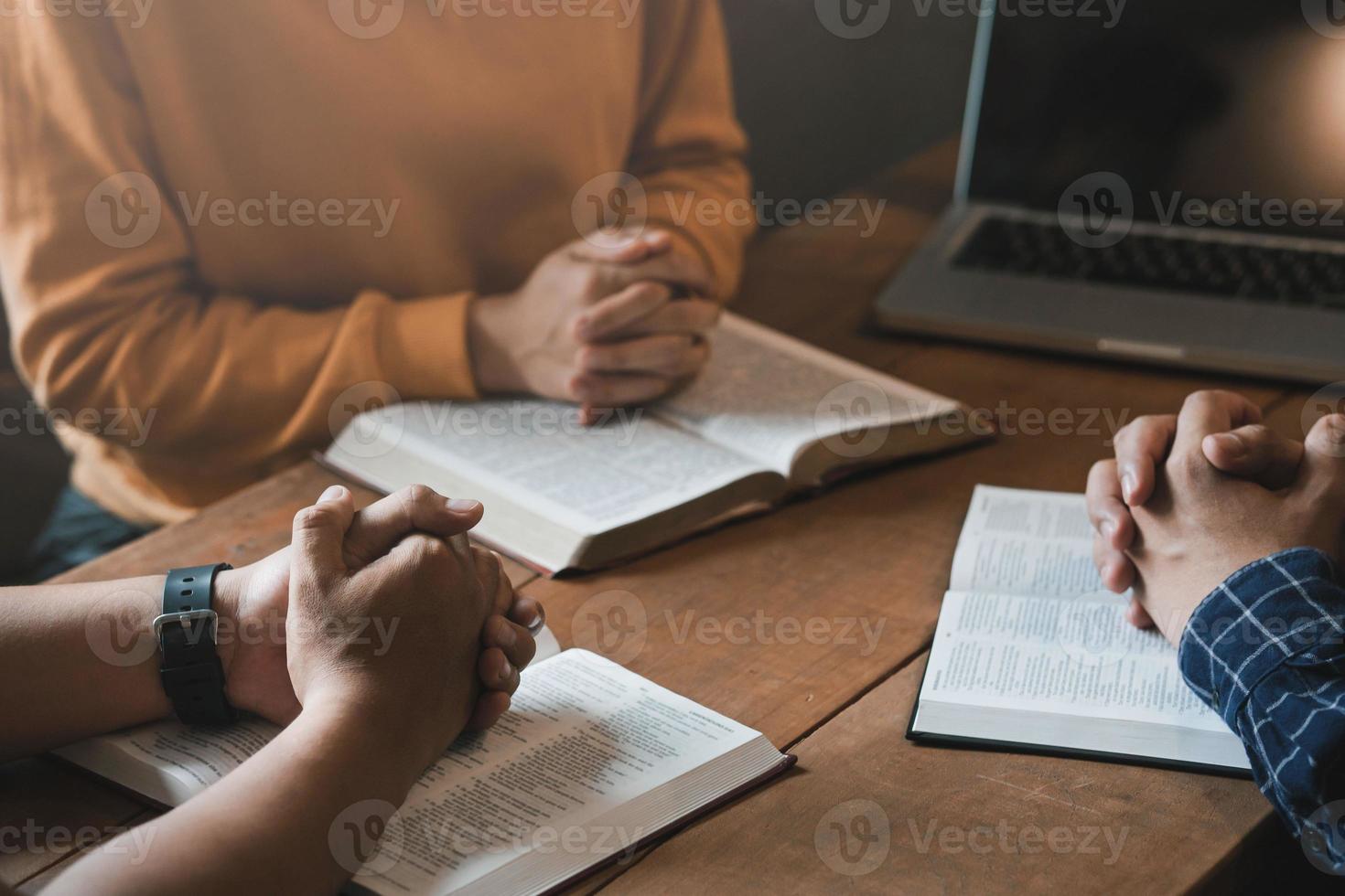 un groupe de chrétiens s'assoient ensemble et prient autour d'une table en bois avec des pages bibliques ouvertes floues dans leur classe. prière pour les frères, foi, espoir, amour, réunion de prière photo