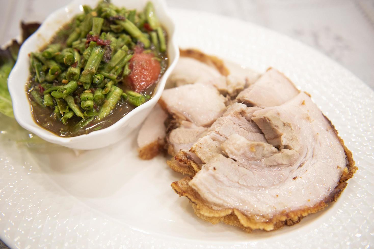 salade épicée de haricots longs et de porc croustillant tranché sur une assiette blanche et de légumes thaïlandais, salade de haricots de porc croustillants photo