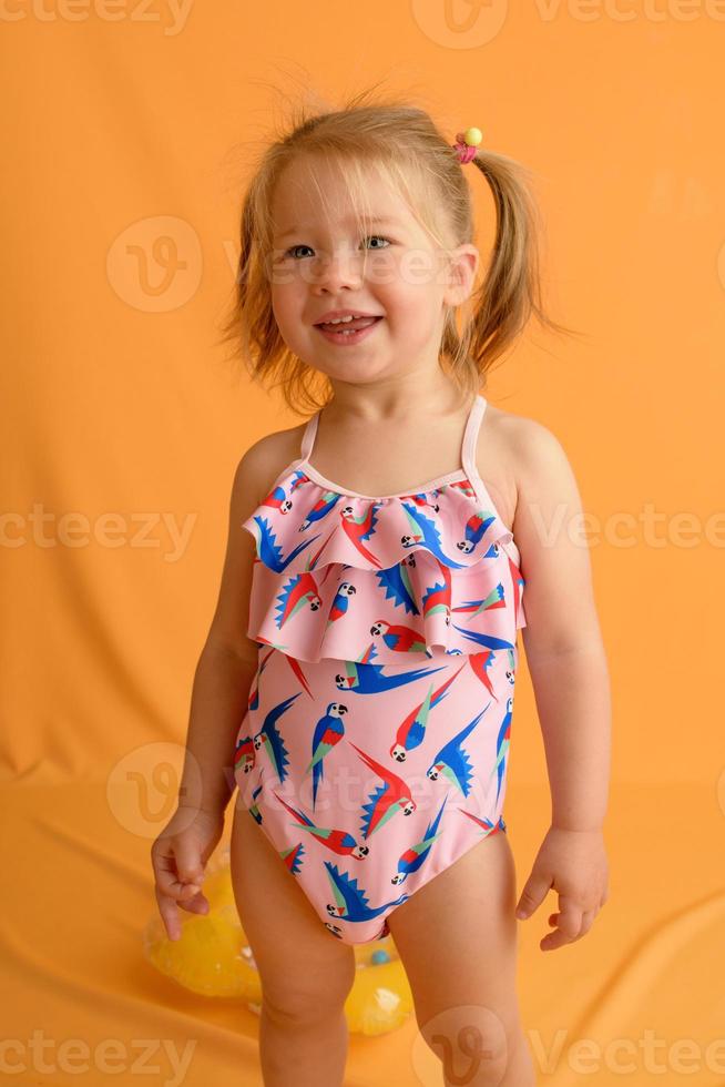 une petite fille vêtue d'un maillot de bain à l'âge d'un an et demi saute ou danse. la fille est très contente. photo prise en studio sur fond jaune.