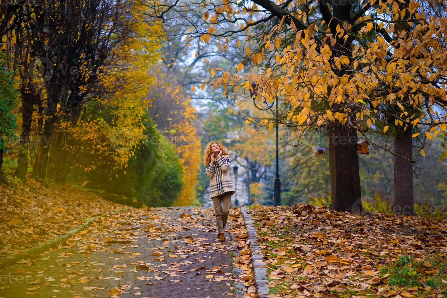 belle fille rousse aux cheveux bouclés et aux yeux bleus. la fille porte une veste à carreaux. la fille est assise sur un banc. photo