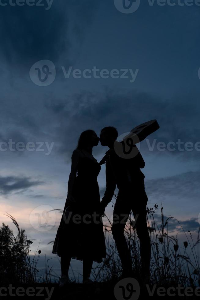 silhouette d'un couple amoureux à une date. l'homme tient la main de la fille. le type aux crabes a une guitare. filmé au coucher du soleil. photo