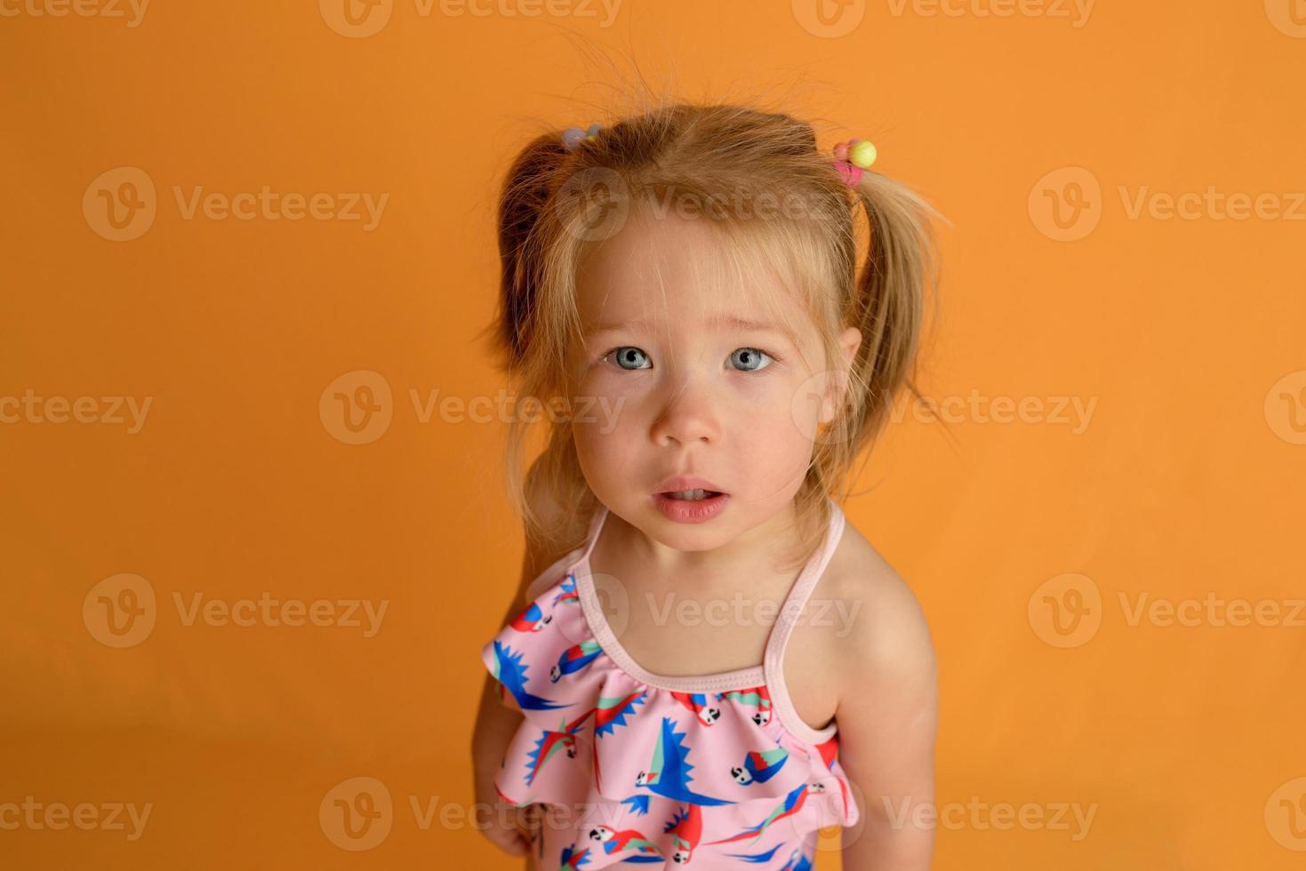 une petite fille vêtue d'un maillot de bain à l'âge d'un an et demi saute ou danse. la fille est très contente. photo prise en studio sur fond jaune.