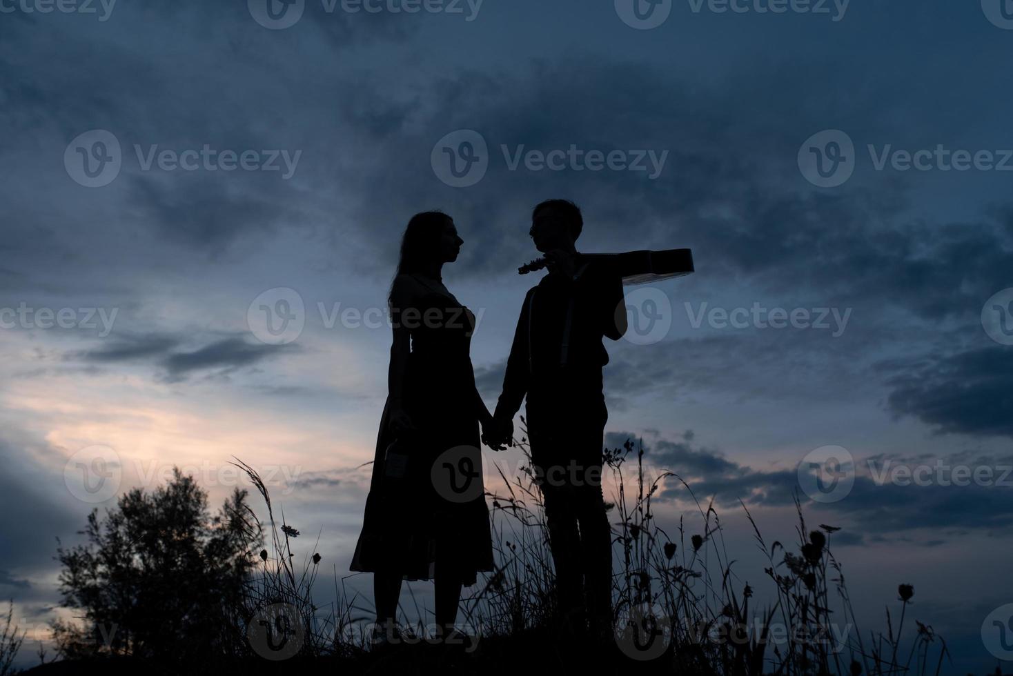 silhouette d'un couple amoureux à une date. l'homme tient la main de la fille. le type aux crabes a une guitare. filmé au coucher du soleil. photo