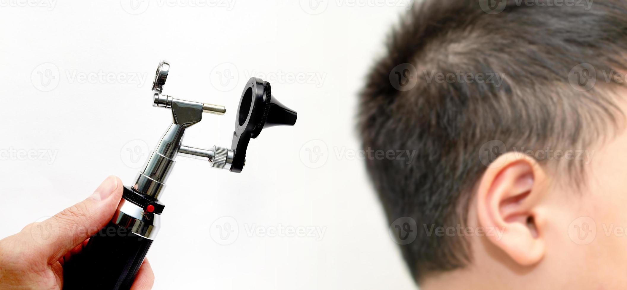 La main tient l'otoscope pour l'examen de l'oreille du médecin ORL sur le cône de la tête de l'oreille sur fond blanc photo