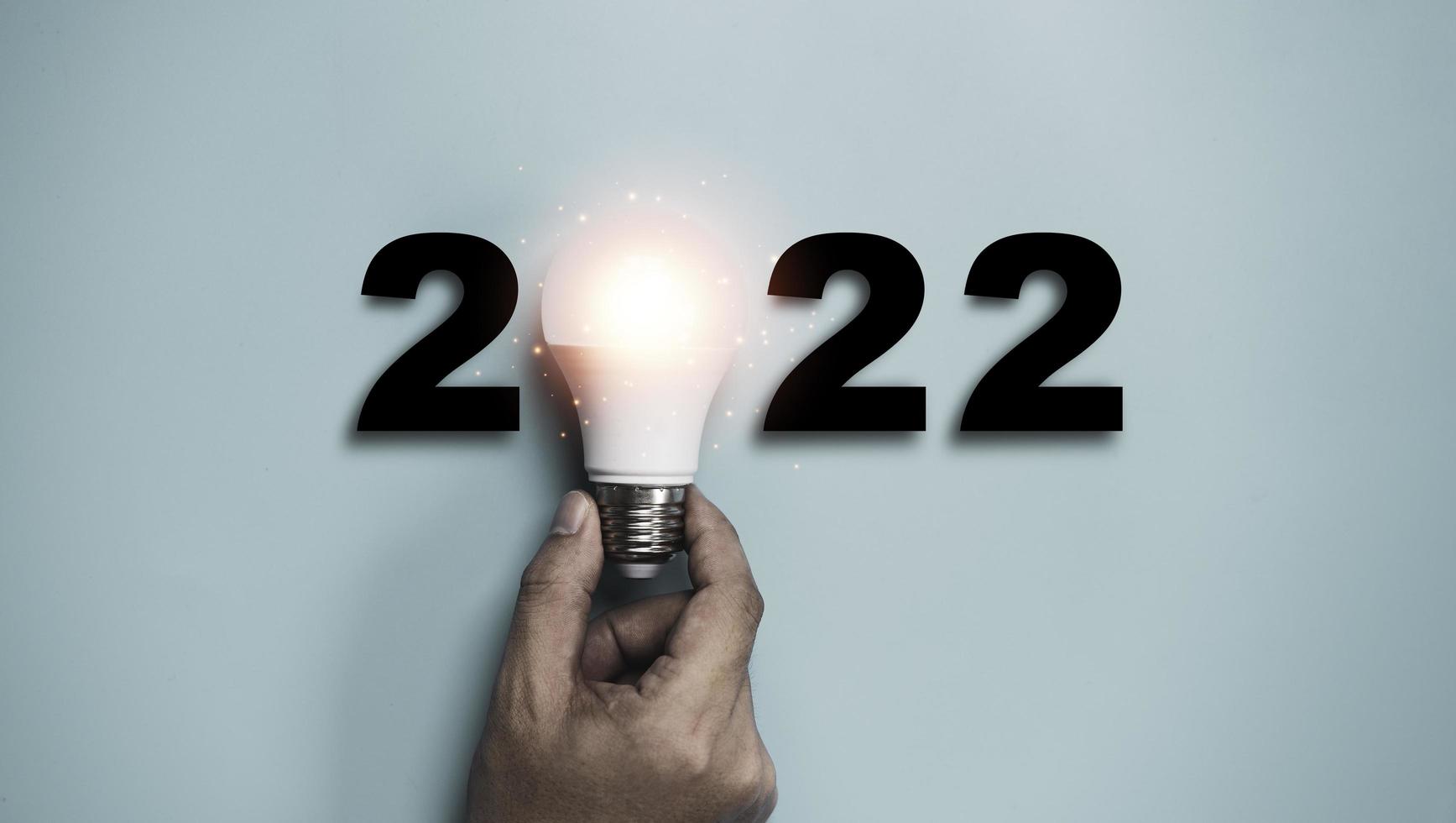 main tenant une ampoule avec 2022 ans pour une idée de bonne année et un concept de pensée créative. photo