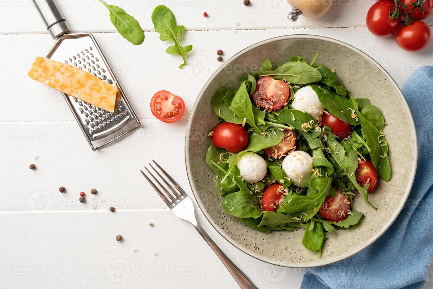 salade fraîche avec roquette, tomates cerises, fromage mozzarella et fromage à pâte dure sur fond de bois blanc. vue de dessus photo