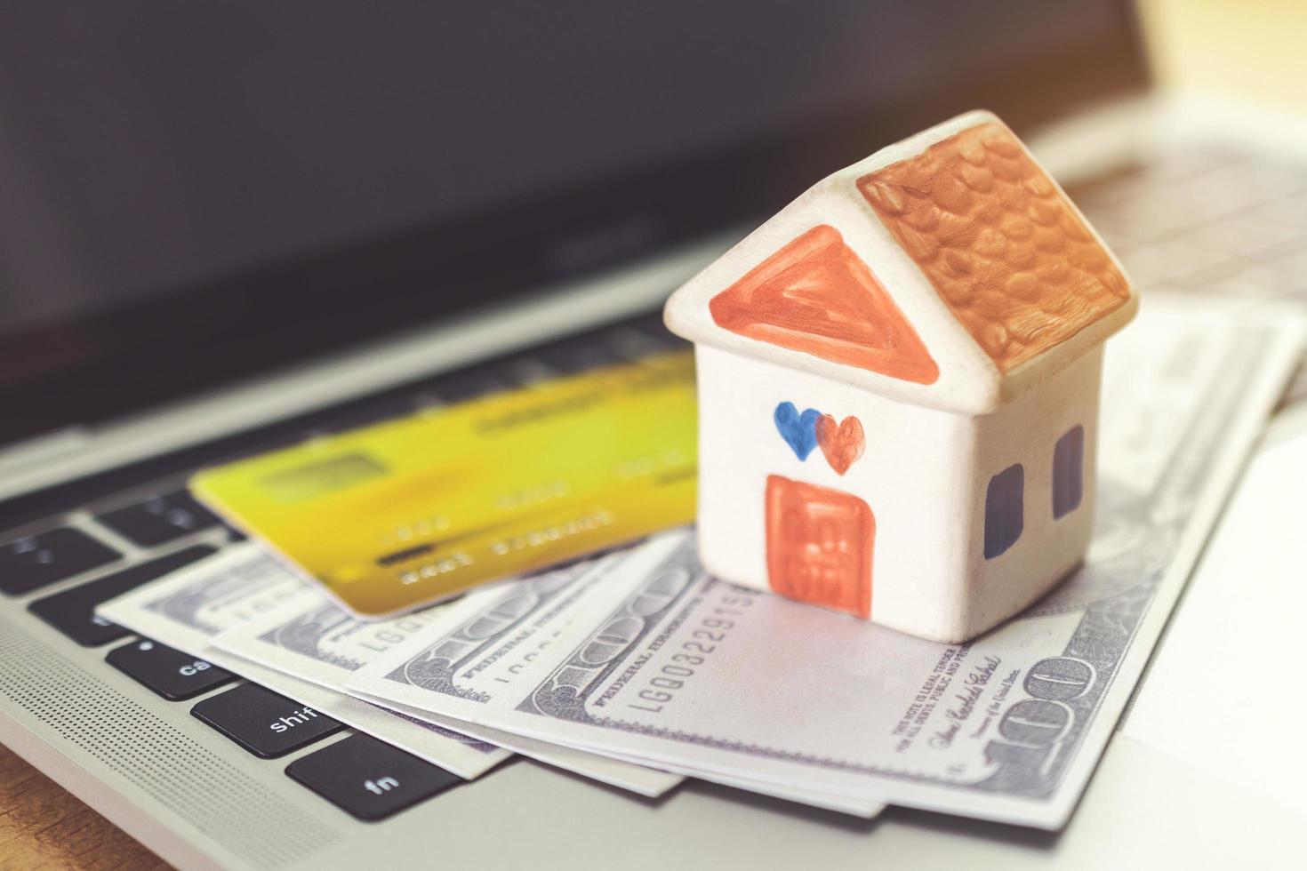 carte de crédit, modèle de maison et cahier sur un bureau en bois. achats en ligne et paiement de la maison à l'aide d'un ordinateur portable photo