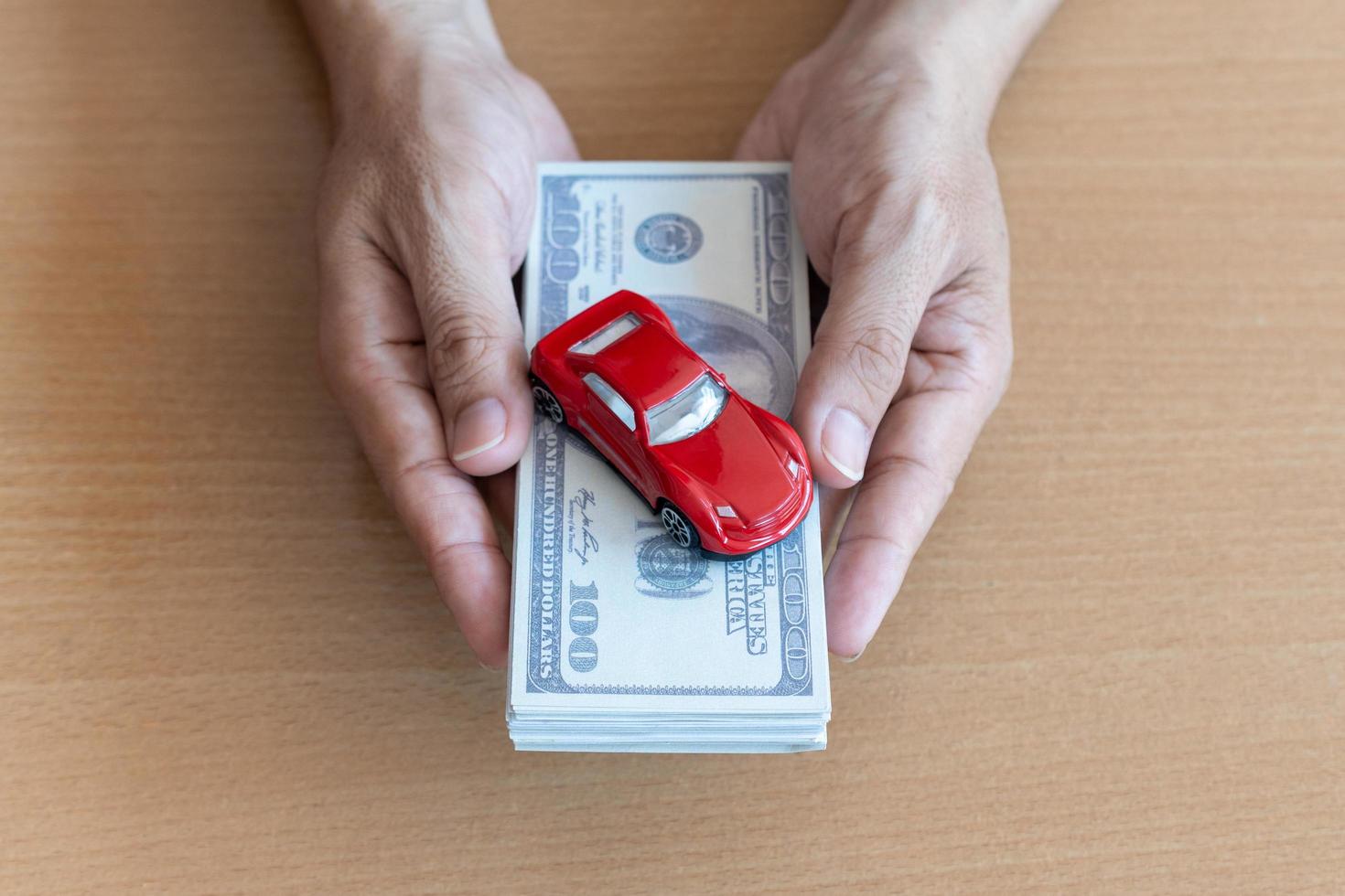 mains d'homme tenant des billets de 100 dollars et une voiture rouge sur une table en bois. remboursement en espèces et concept financier photo