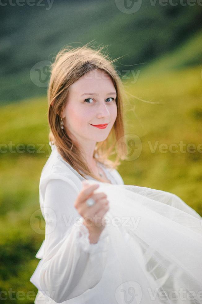 femme en robe de mariée traverse le champ vers les montagnes photo