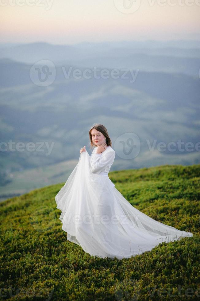 femme en robe de mariée traverse le champ vers les montagnes photo