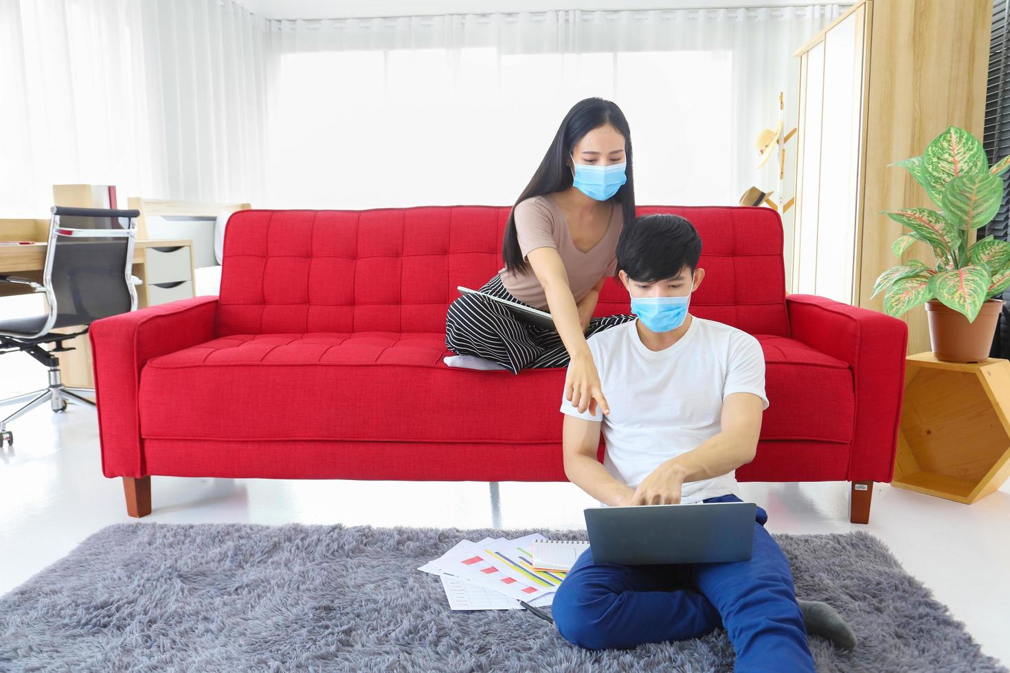 jeune couple portant un masque facial travaillant à domicile pendant la quarantaine du coronavirus ou de la pandémie de covid-19 en tant que nouvelle politique normale mise en œuvre photo