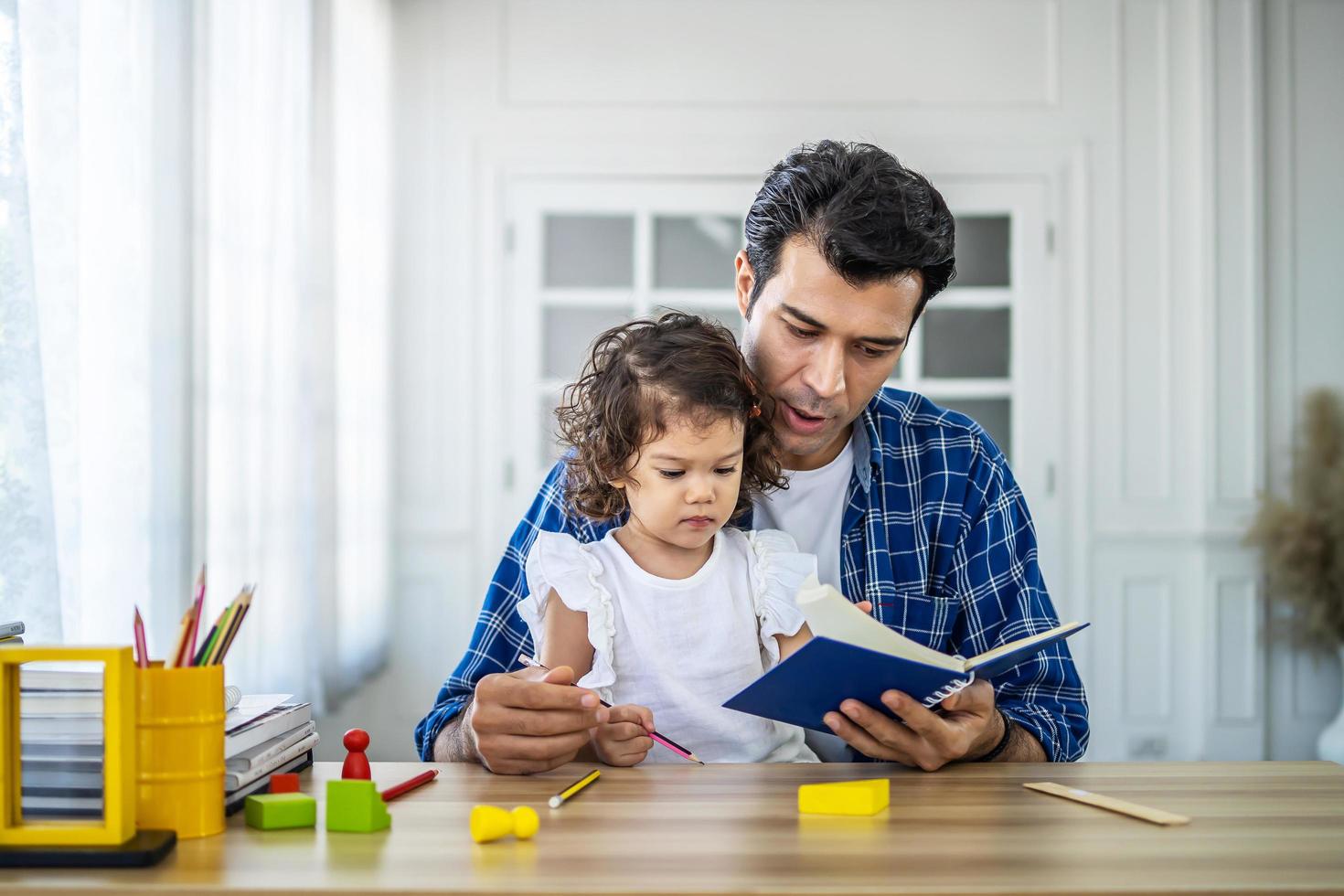 portrait d'un jeune père enseignant l'étude de ses jolies petites filles. petite fille souriante et excitée appréciant l'apprentissage avec un père agréable à la maison. éducation des enfants, concept d'enseignement à domicile photo