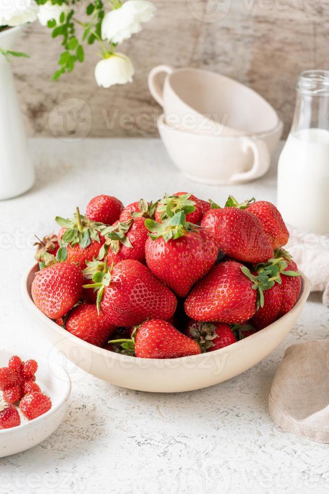 bol avec fraise sur tableau blanc, bouteille de lait, fleur. photo de nature morte avec des baies d'été