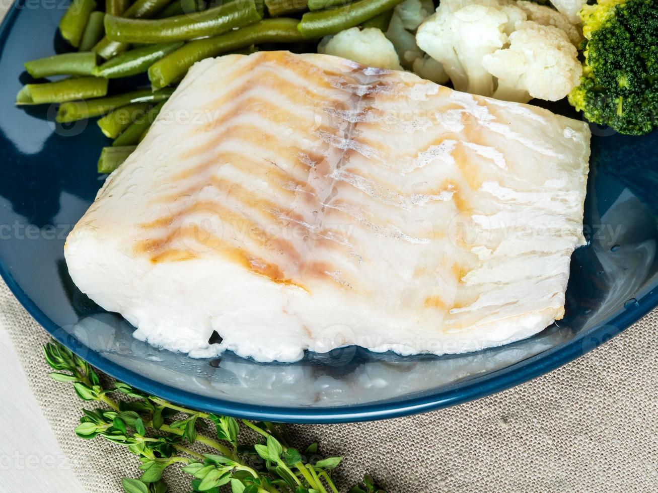 filet de morue de poisson de mer cuit au four avec légumes sur plaque bleue, serviette grise, vue latérale, gros plan. régime équilibré photo