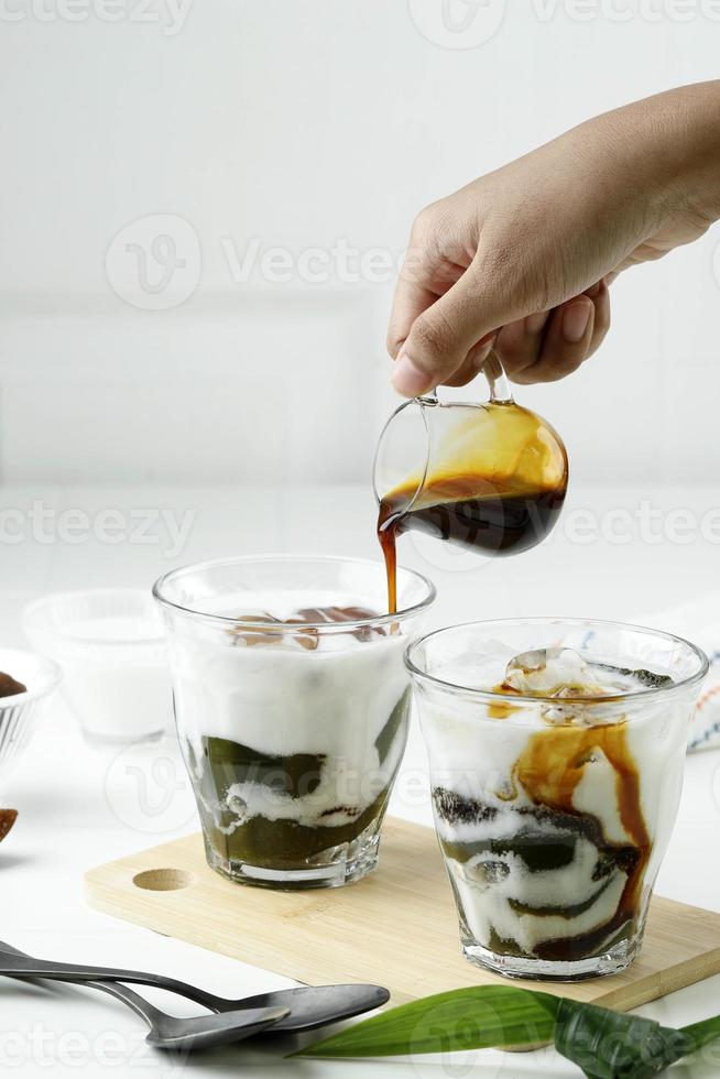 versez du sucre de palme liquide dans le verre avec de la gelée d'herbe verte ou du cingcau hijau. cincau ijo est une cuisine de rue populaire d'indonésie photo