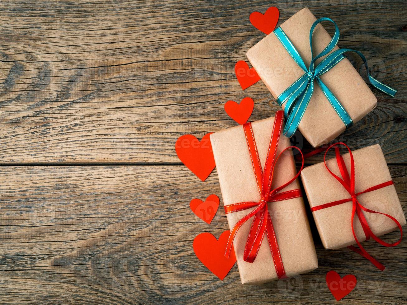 fond de la saint-valentin. cadeaux emballés avec du papier kraft brun, avec des rubans rouges, des coeurs sur fond de bois ancien vintage rustique vieilli photo