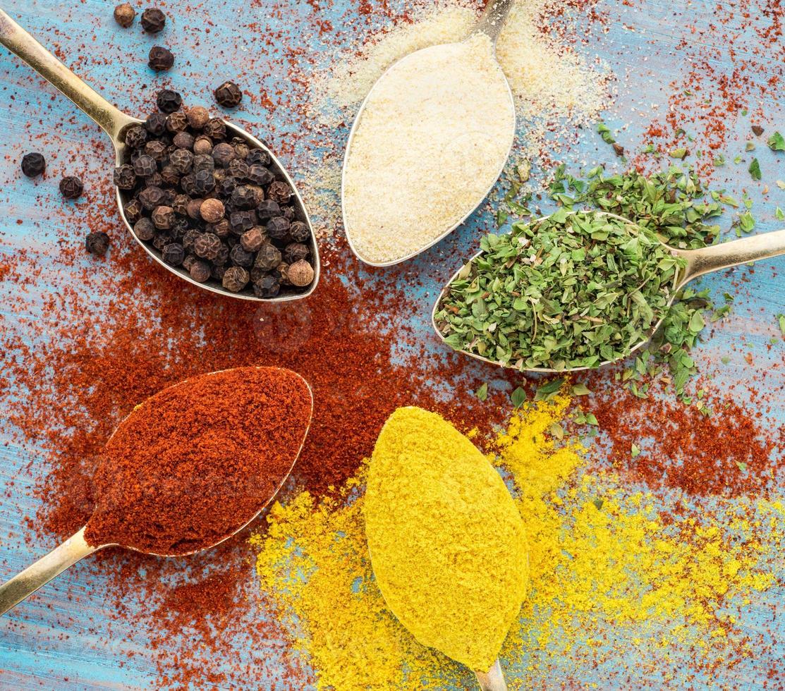 épices moulues - ail, curcuma, paprika, origan. ronde de cuillères dorées sur une table en bois bleue. vue de dessus, gros plan photo