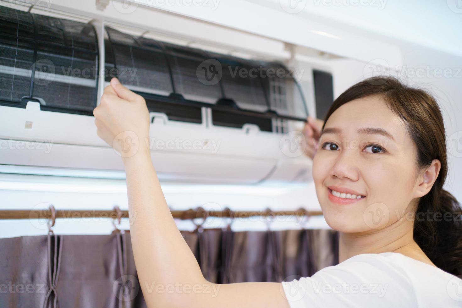 femme asiatique nettoyant un filtre de climatisation sale et poussiéreux dans sa maison. femme au foyer enlevant un filtre de climatiseur poussiéreux. photo