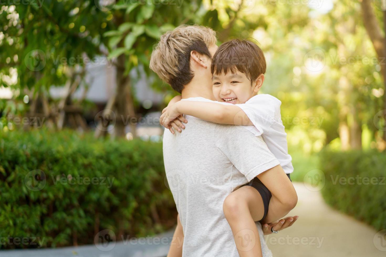 un petit garçon asiatique heureux aime jouer et se promener dans le parc avec papa en gros plan, un garçon asiatique a un beau sourire tout en regardant son père. portrait de petit garçon au parc et à l'aire de jeux. photo