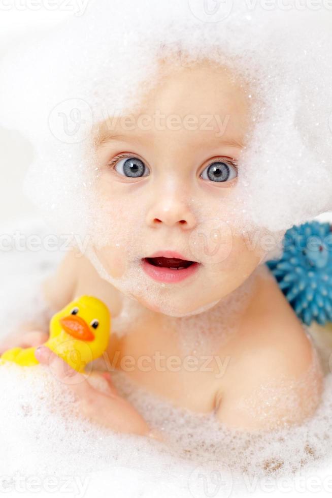 photo de bébé dans une baignoire avec canard en caoutchouc et mousse de bain sur le visage