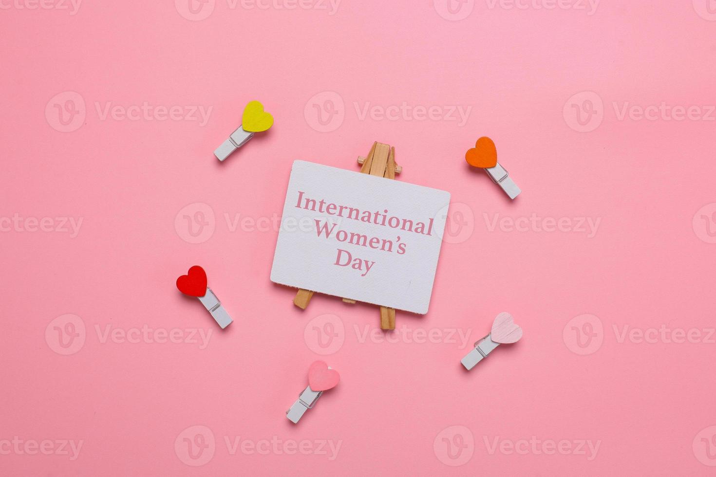 mise à plat de la journée internationale de la femme écrit sur une pancarte entourée de mini coeurs sur des pinces à linge sur fond rose photo