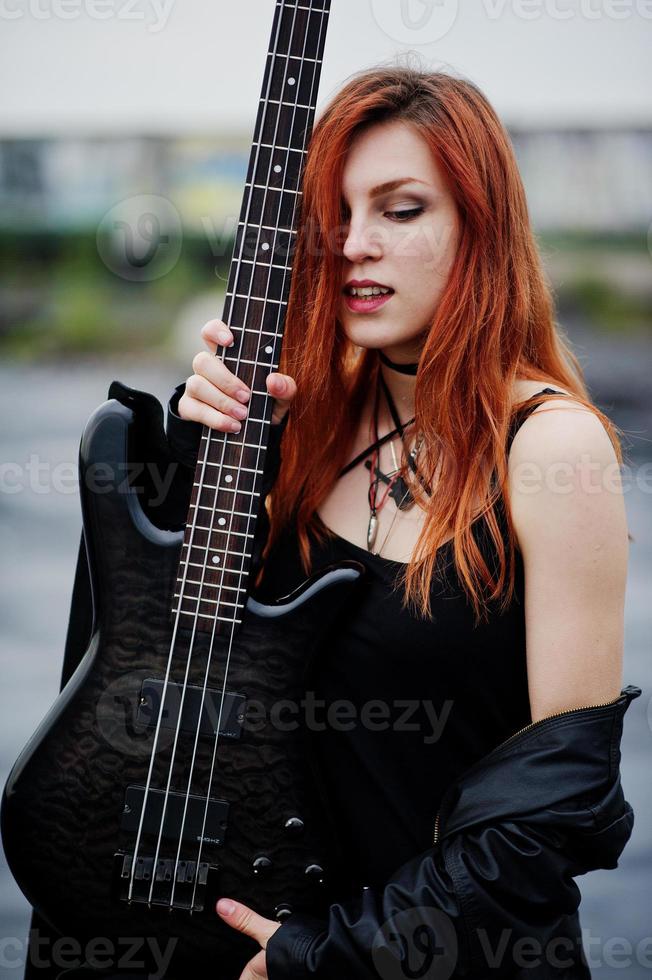 fille punk aux cheveux rouges sur fond noir avec guitare basse sur le toit. photo