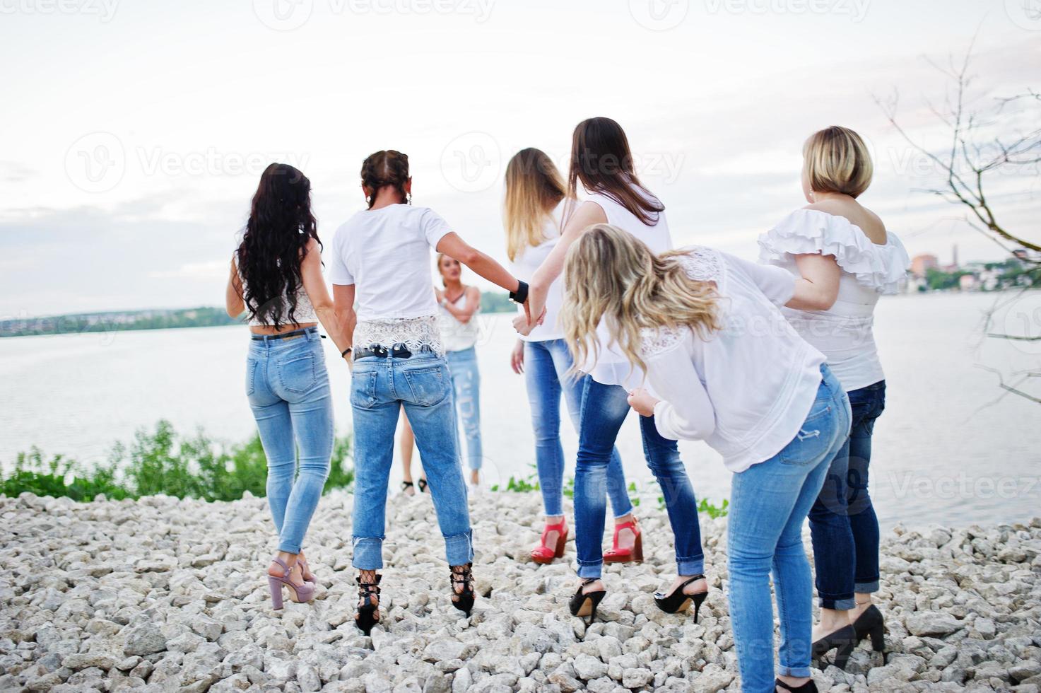 les demoiselles d'honneur portant des jeans et des t-shirts blancs regardent le lac lors de l'enterrement de vie de jeune fille. photo