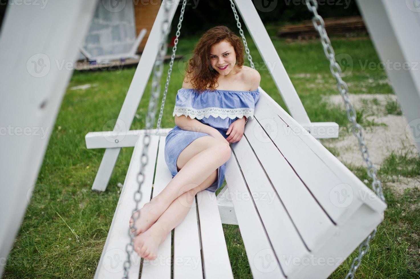 portrait d'une superbe jeune fille vêtue d'une robe bleue de style marin assise sur des balançoires au bord du lac. photo