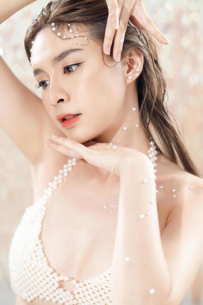 belle jeune femme asiatique avec une peau fraîche et propre avec des perles sur fond de paillettes. soins du visage, soins du visage, beauté et spa, joli portrait de femmes asiatiques. photo