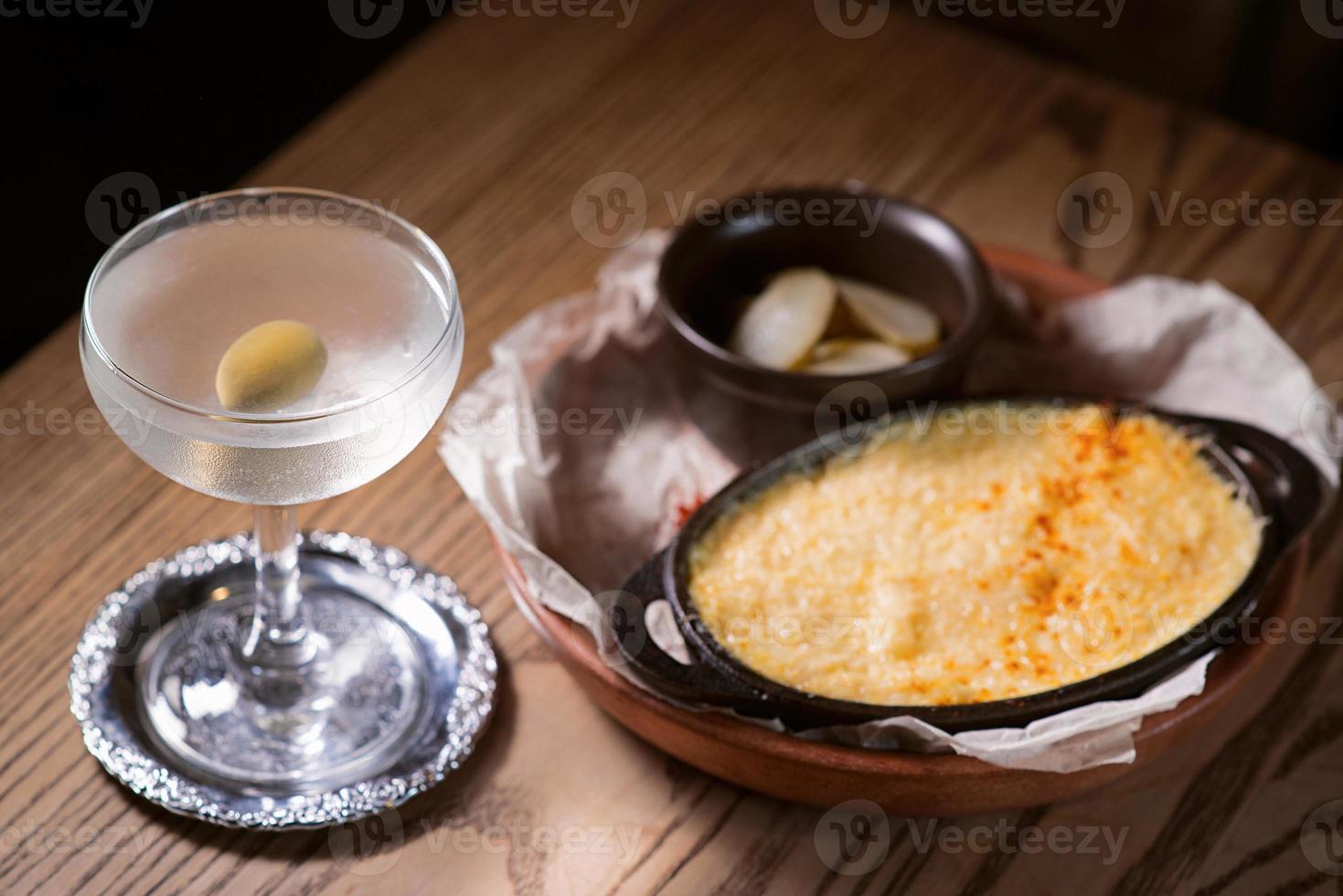 poisson cuit au four avec du fromage et des concombres salés et cocktail d'alcool avec olive sur la table photo