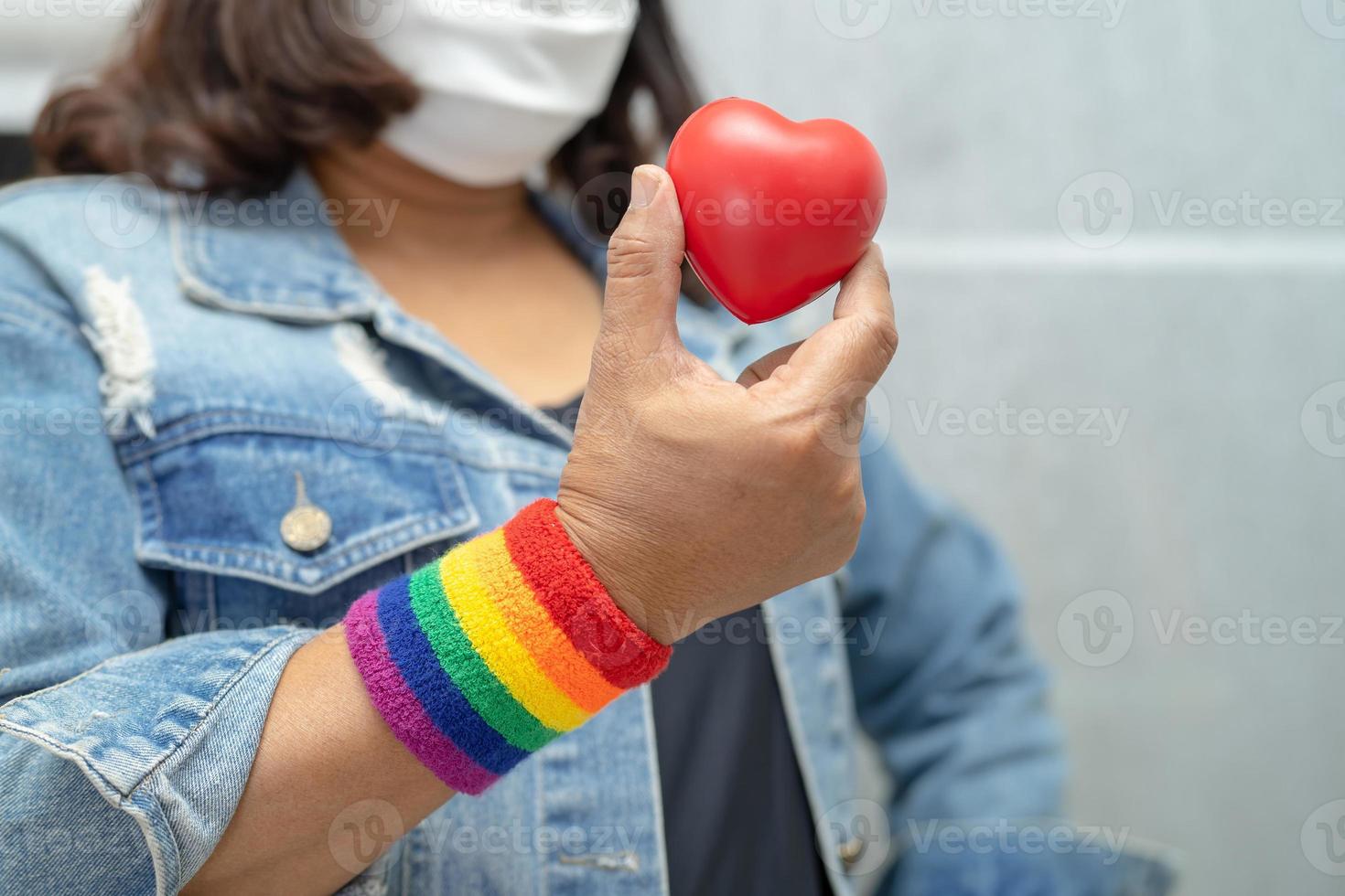 une dame asiatique portant des bracelets de drapeau arc-en-ciel et tenant un coeur rouge, symbole du mois de la fierté lgbt célèbre chaque année en juin les droits des gays, lesbiennes, bisexuels, transgenres et humains. photo