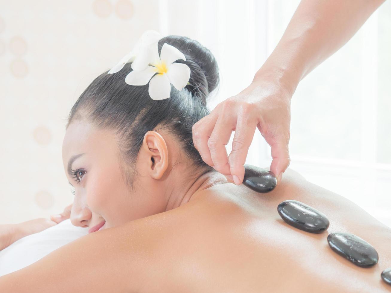 une belle femme asiatique se détend dans un magasin de spa lorsqu'une masseuse experte place une pierre chaude sur son dos photo