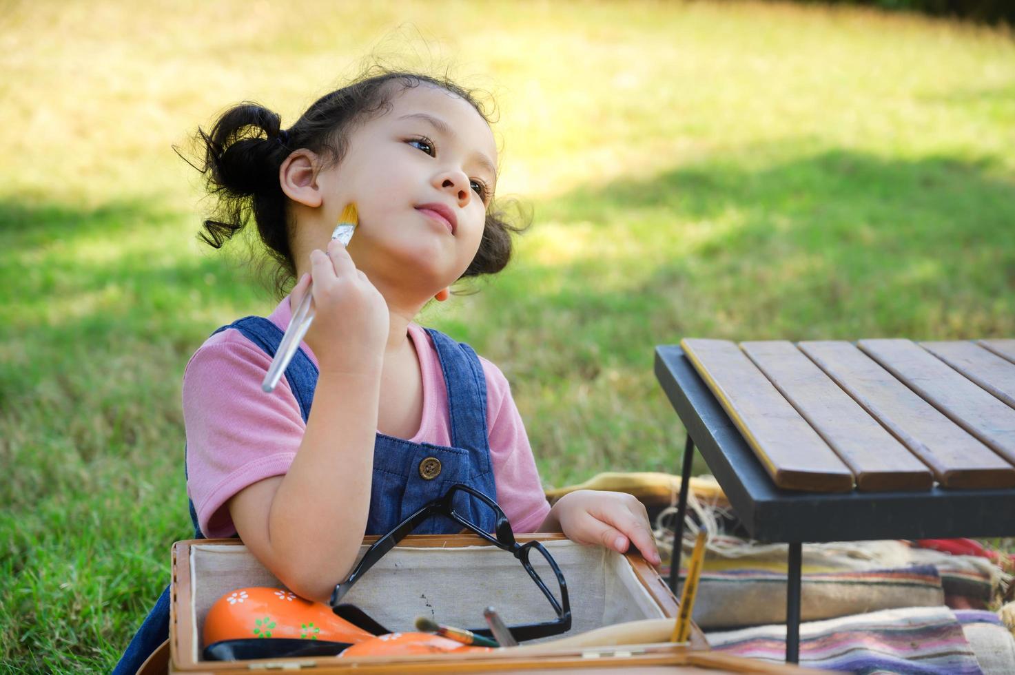 une petite fille est assise sur le tissu et peinte sur le visage, participe à l'apprentissage et joue à l'extérieur de l'école dans le parc naturel photo