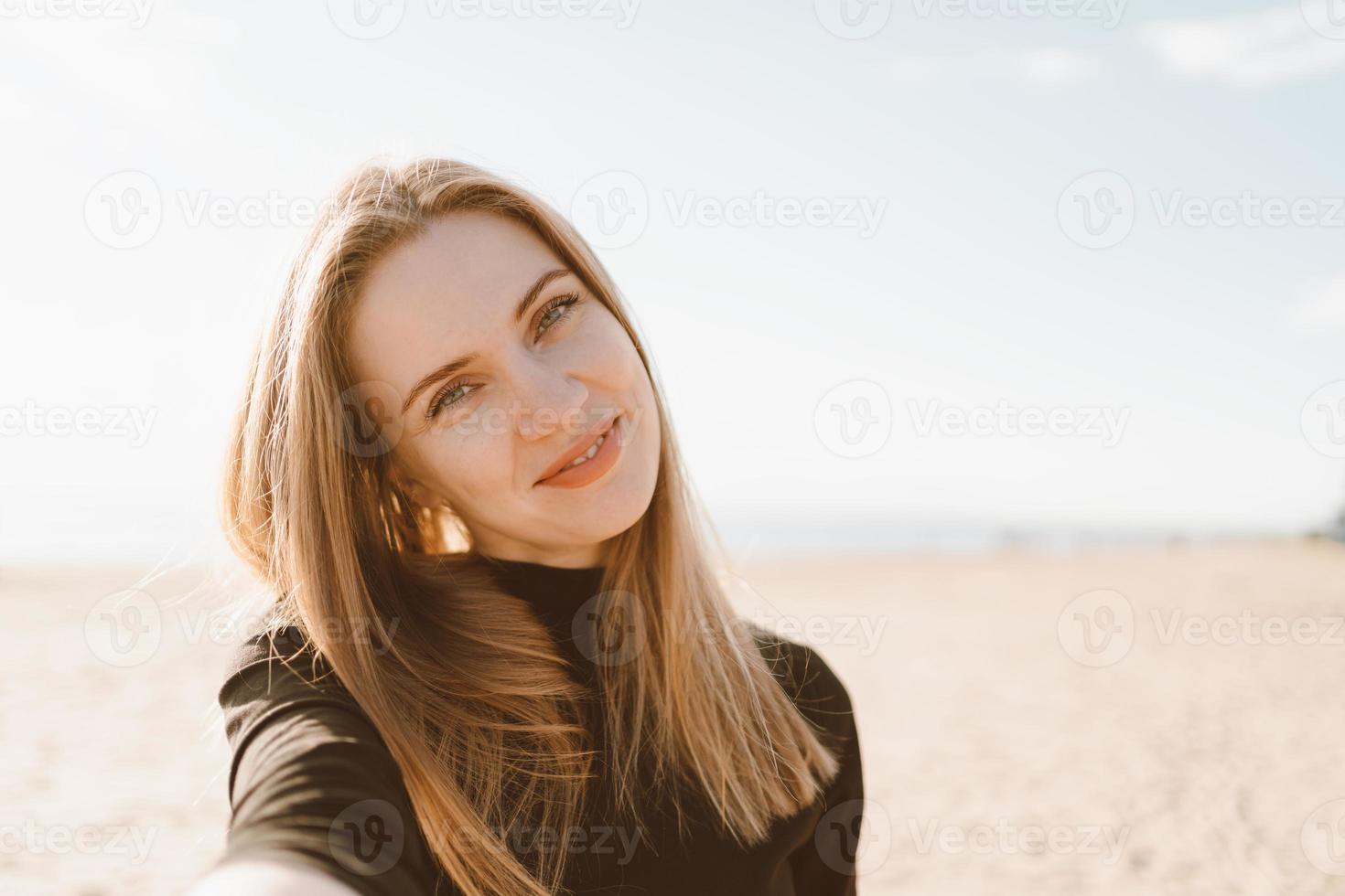 jolie femme aux cheveux longs prend selfie sur smartphone sur la plage en été ou en automne. photo