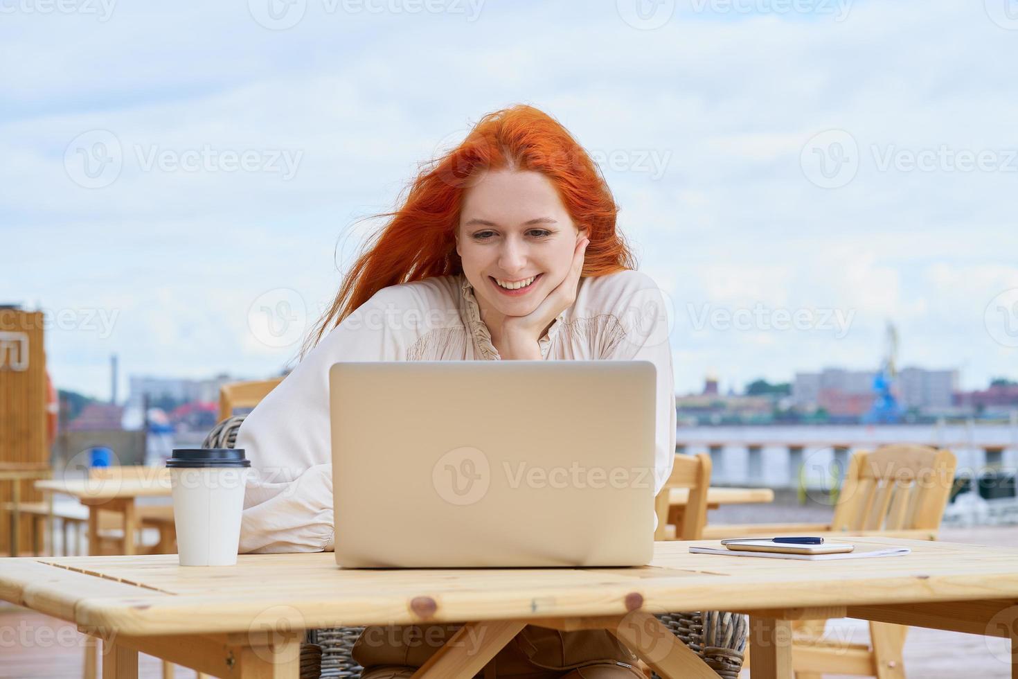 femme indépendante assise dans un café dans la rue et travaillant à distance sur un ordinateur portable. cours d'écoute pour étudiantes photo