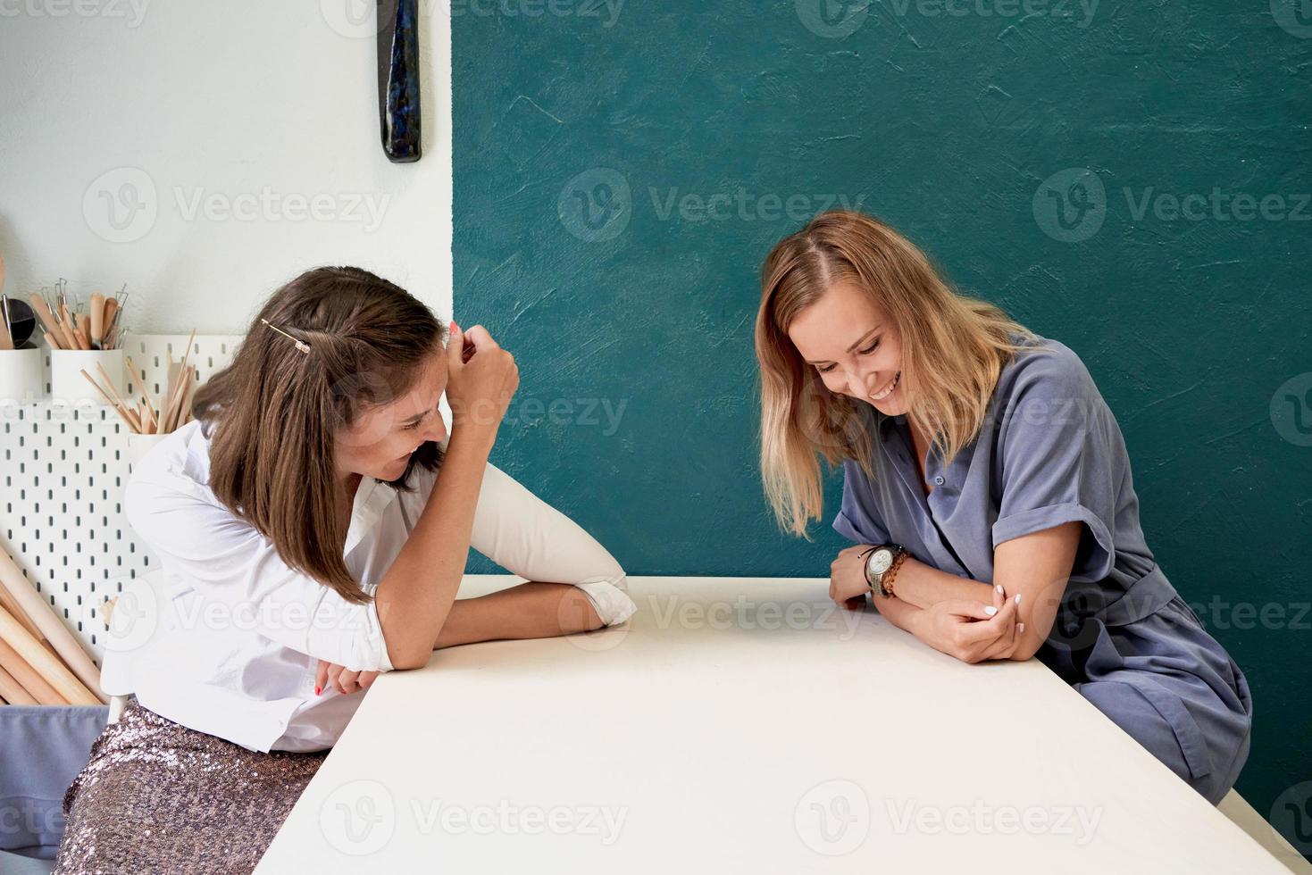 deux belles femmes rient. femme d'affaires s'asseoir à table sur le lieu de travail et parler, s'amuser photo