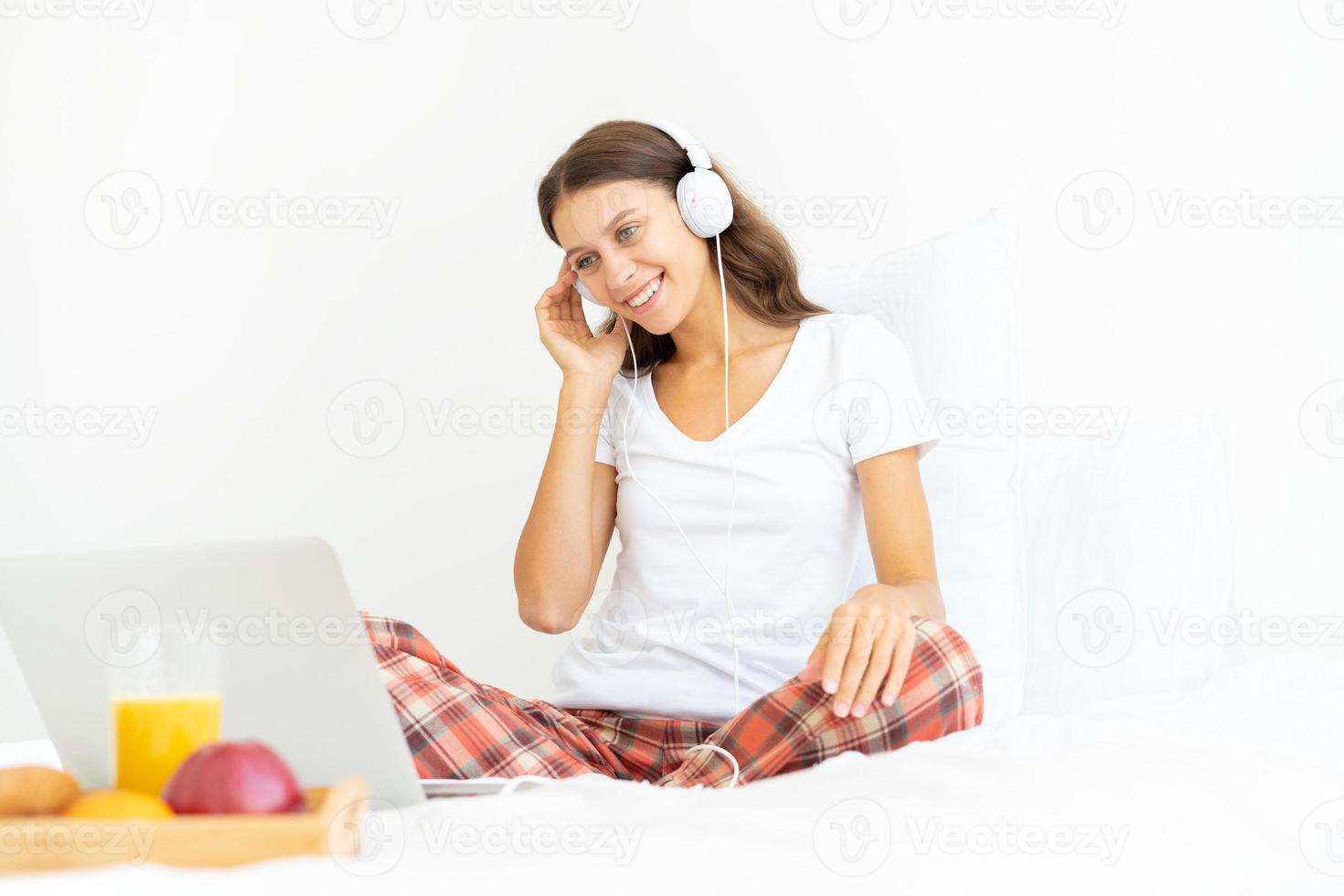 jeune femme souriante assise sur le lit dans la chambre et écoutant de la musique ou regardant un film photo