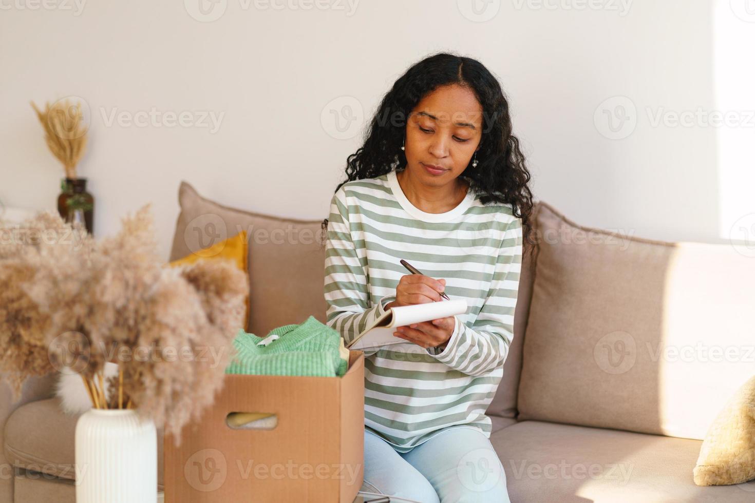 une femme afro-américaine compte les vêtements dans une boîte en carton. déménager et emballer photo