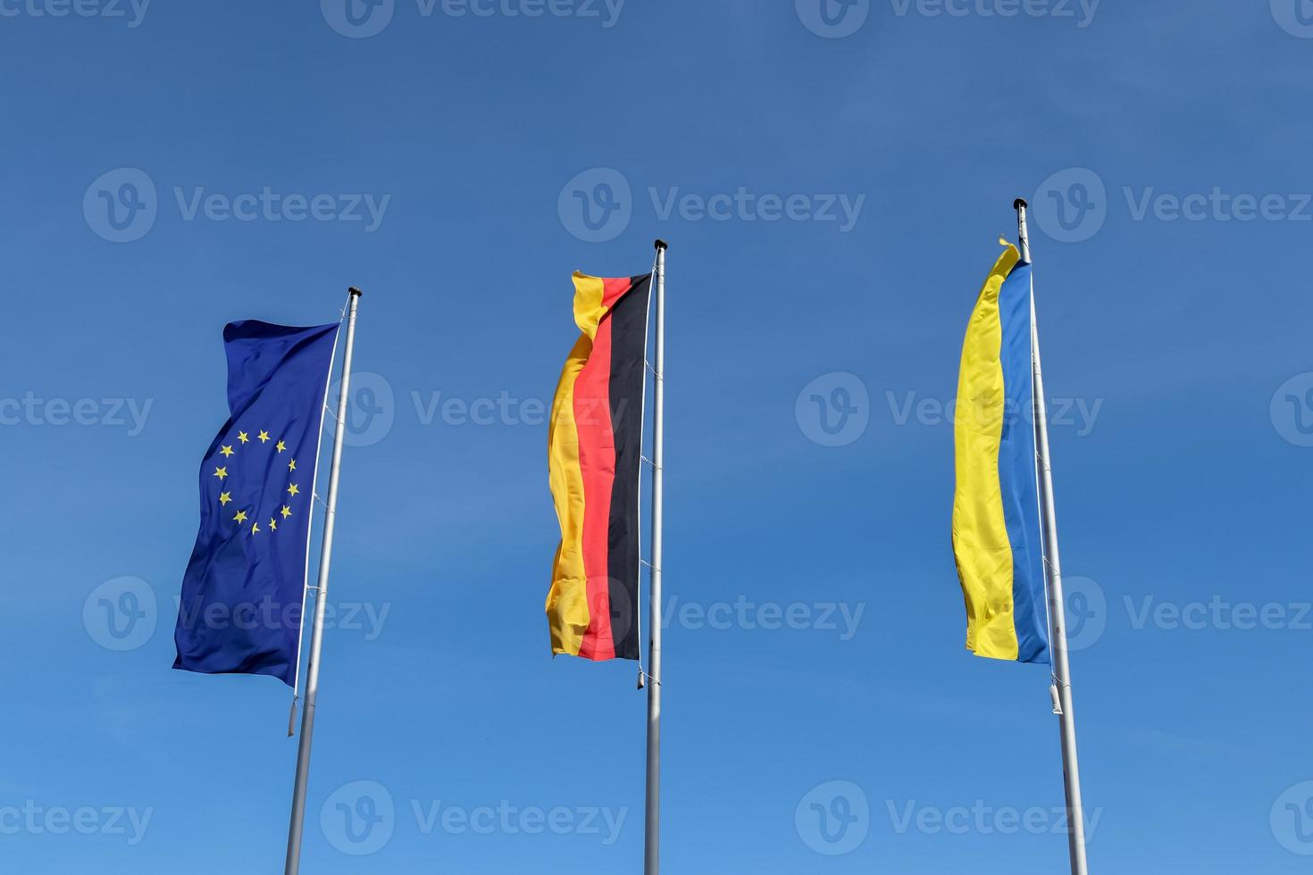 les drapeaux de l'ukraine, de l'allemagne et de l'union européenne volent côte à côte contre le ciel bleu. photo