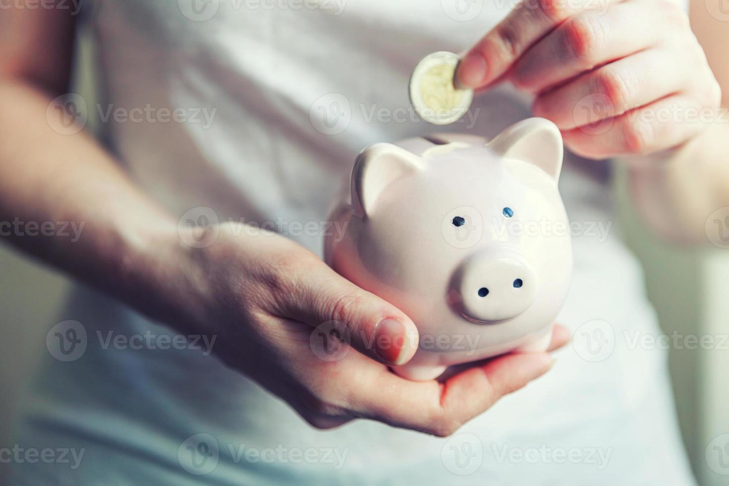 mains de femme tenant une tirelire rose et mettant de l'argent pièce en euro photo