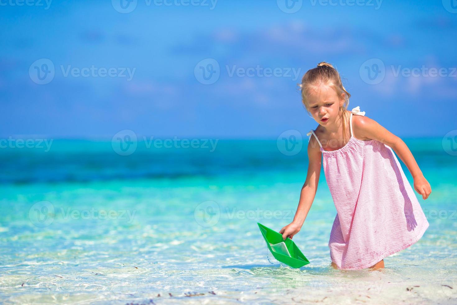 adorable petite fille jouant avec un bateau en papier dans une mer turquoise photo