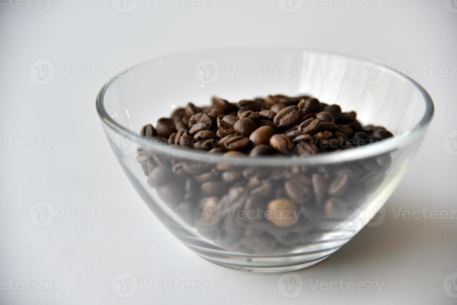 Grains de café dans un bol en verre sur fond blanc photo