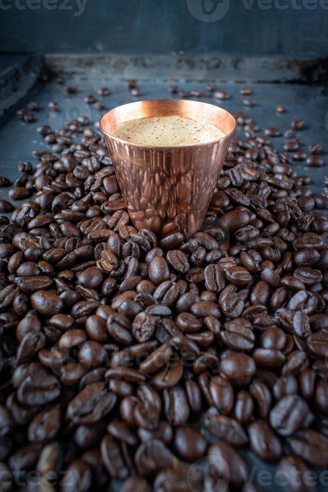 tasse en cuivre remplie de café expresso au centre de grains de café crus étalés sur une table rustique photo