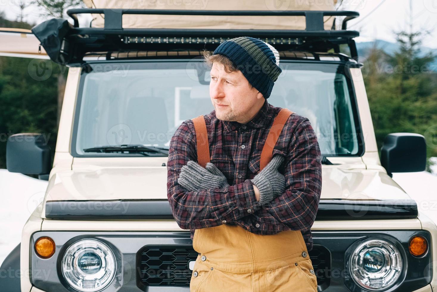 portrait d'un homme en vêtements d'hiver debout près de sa voiture et profitant d'une journée enneigée près de la forêt photo