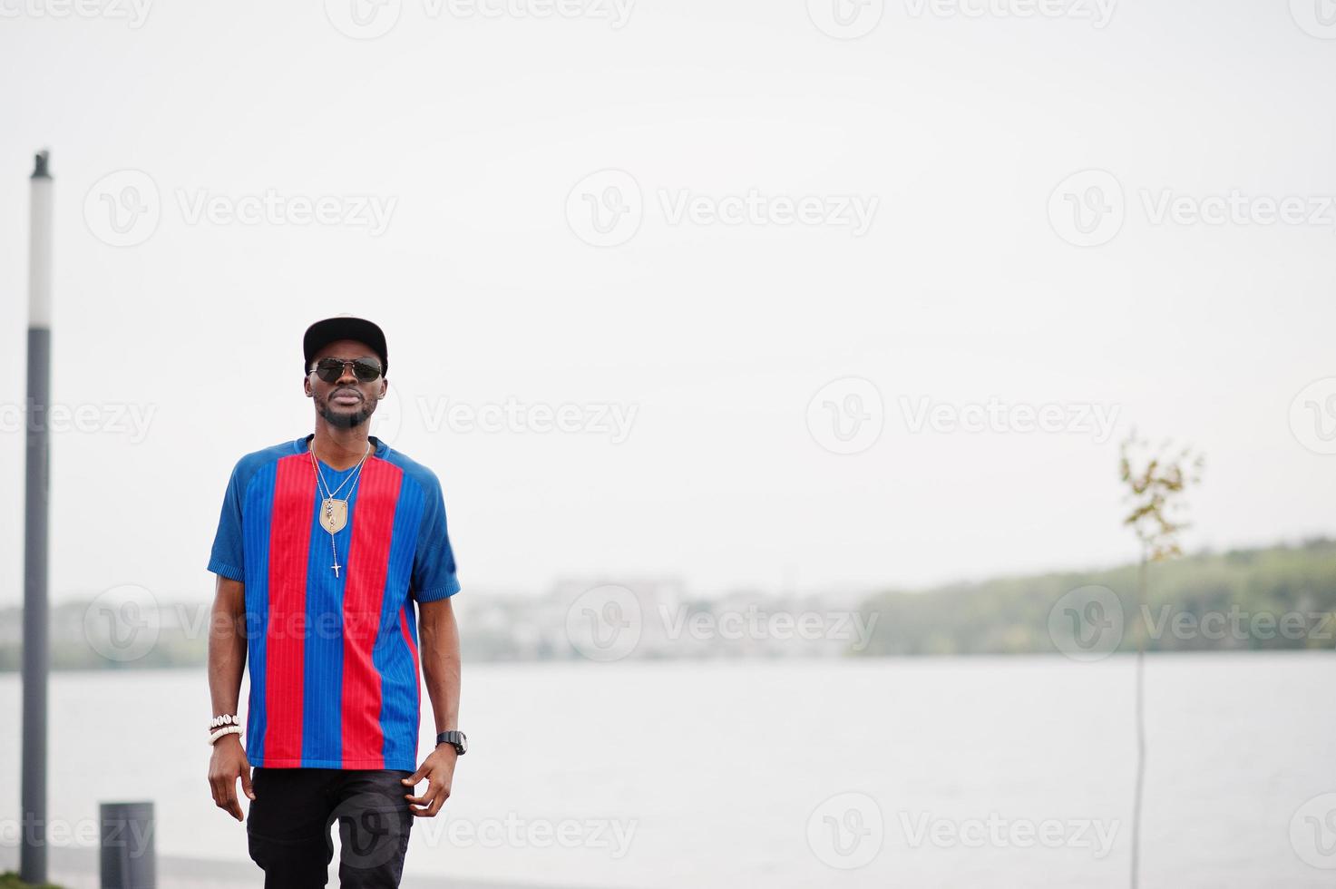 garçon afro-américain élégant portant une casquette, un t-shirt de football et des lunettes de soleil. portrait d'homme sportif noir. photo