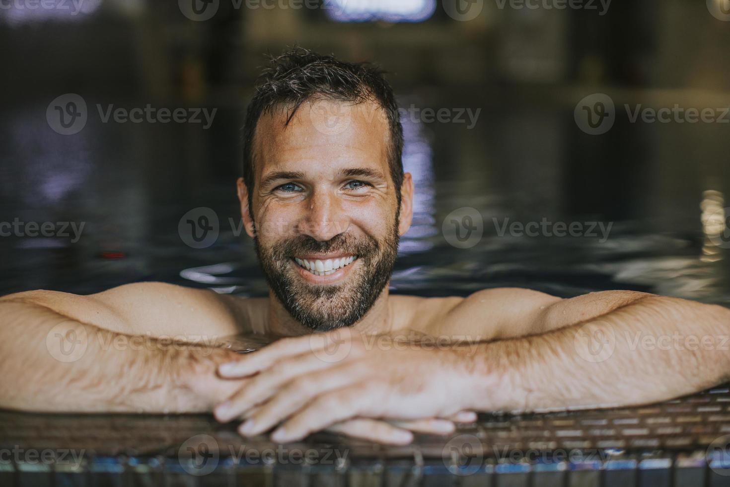 portrait d'un jeune homme souriant se relaxant au bord de la piscine photo